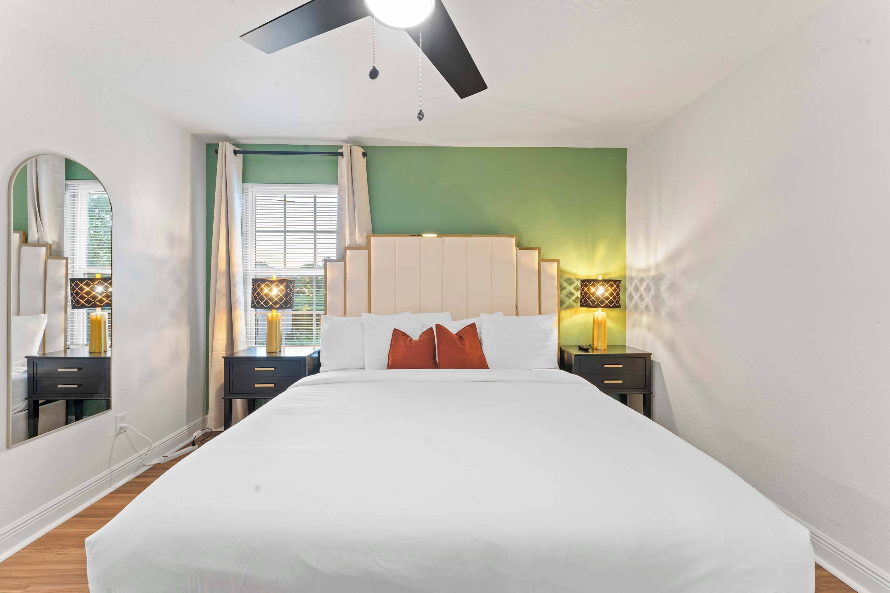 A hotel room with a large bed, a ceiling fan, a nightstand with a lamp, and a window with curtains.