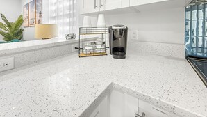 A modern kitchen with white cabinetry, a coffee maker, and a sugar and coffee station.