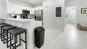 A modern kitchen with white cabinets, stainless steel appliances, and a bar area with stools.