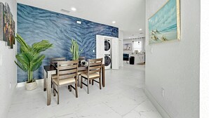 A modern kitchen with white cabinets, a built-in oven, and a dining area with a marble floor and wooden chairs.