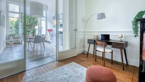 En moderne stue med en glasdør, der fører ud til en balkon, et spiseområde og et arbejdsområde med skrivebord og stol.