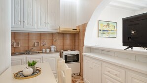 A kitchen with white cabinetry, a built-in oven, a microwave, and a small dining area with a table and chairs. - Apartment 'Le Coq' with Balcony, Wi-Fi and Air Conditioning (Mykonos)
