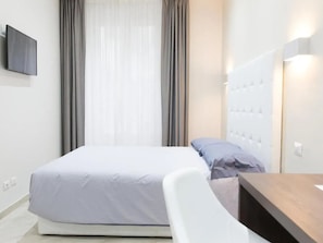 A modern hotel room with a bed, a desk, and a television on the wall.