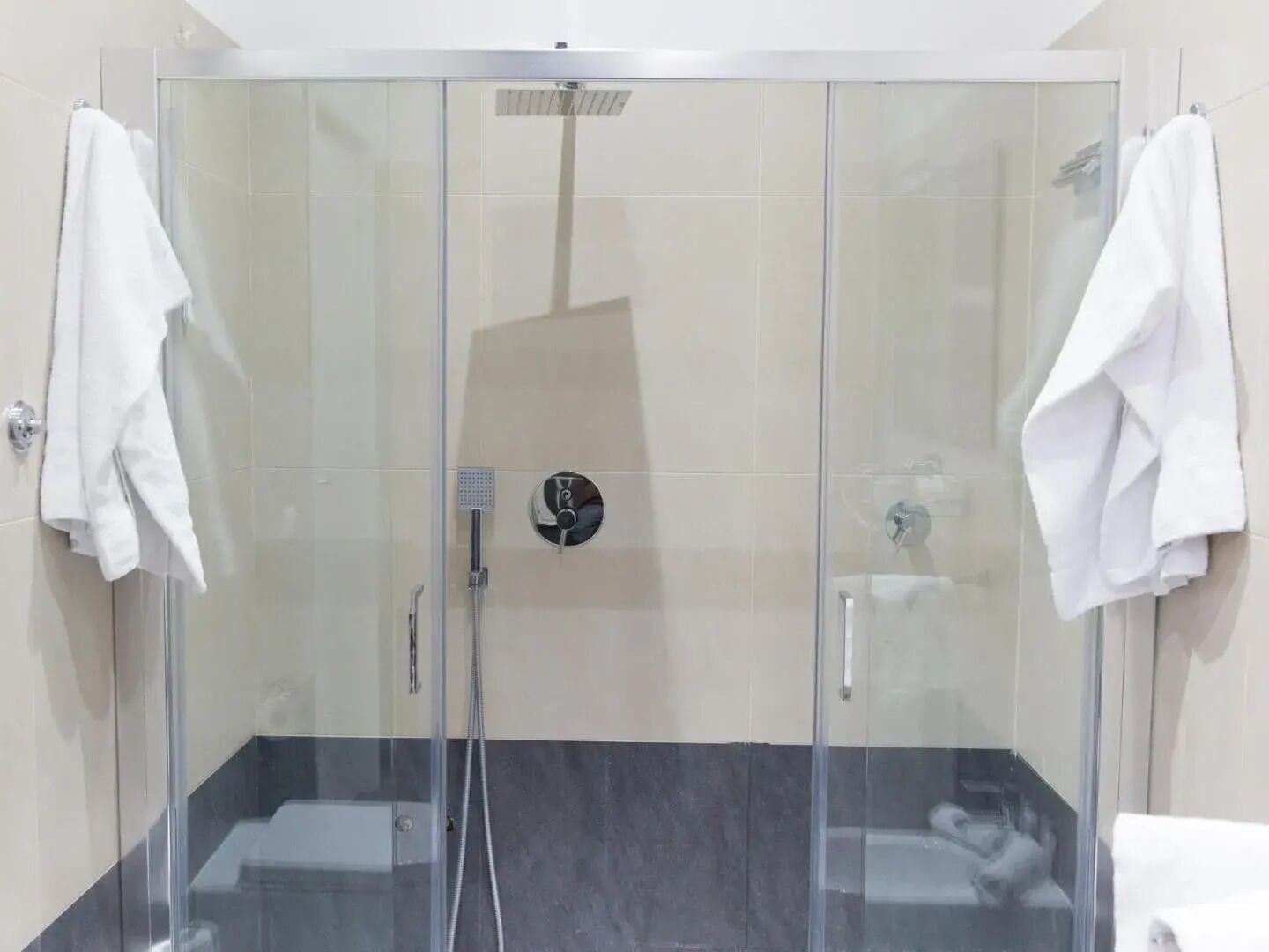 A glass-enclosed shower stall with a handheld showerhead and a wall-mounted control panel.