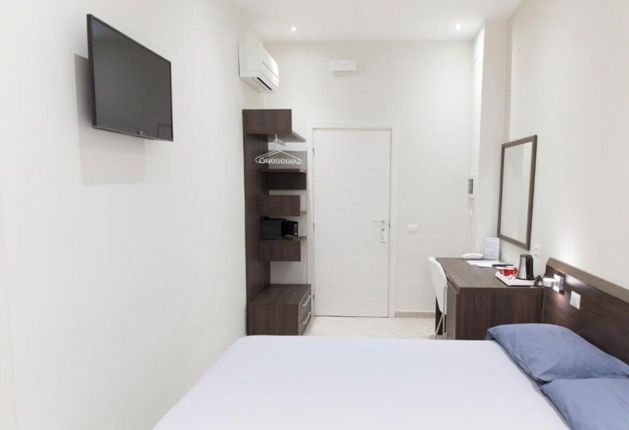 Habitación de hotel moderna con cama, escritorio con silla, televisor de pantalla plana en la pared, armario y puerta.