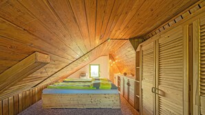 An attic bedroom with a sloped ceiling, wooden walls, a bed with colorful bedding, a wardrobe, and a window providing natural light.