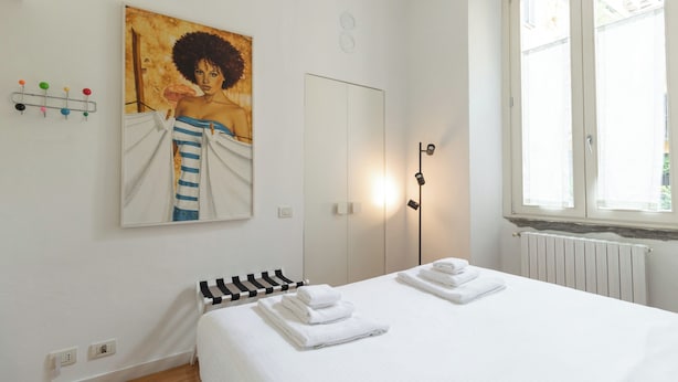 Un dormitorio con cama, toallero en la pared, un cuadro, radiador y ventana.