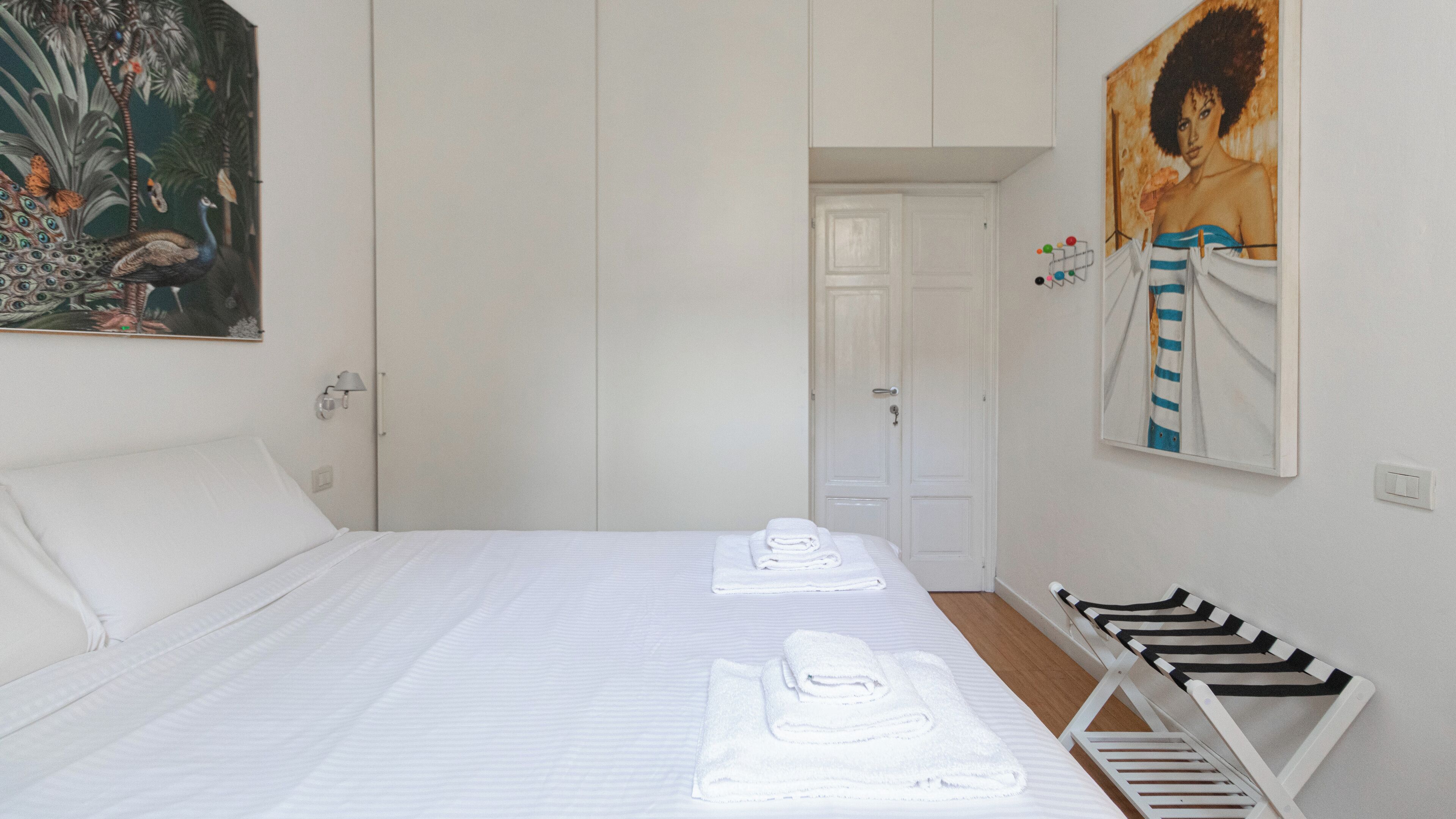 A hotel room with a bed, a set of towels, a painting, and a door.