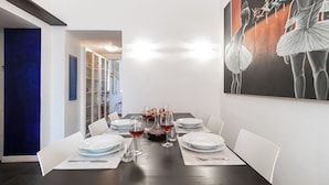 Comedor con mesa preparada para cuatro, copas de vino tinto y un cuadro de bailarinas en la pared.