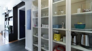 Una cocina con armarios blancos, una puerta azul y diversos electrodomésticos.