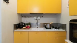 Cocina compacta con armarios amarillos, un lavamanos de acero inoxidable, estufa y microondas.