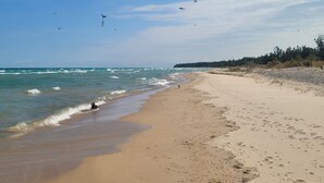 A beach with a sandy shore, waves, and birds flying in the sky. - A Frame cabin with a short stroll to a gorgeous sandy beach! (Beaver Island)