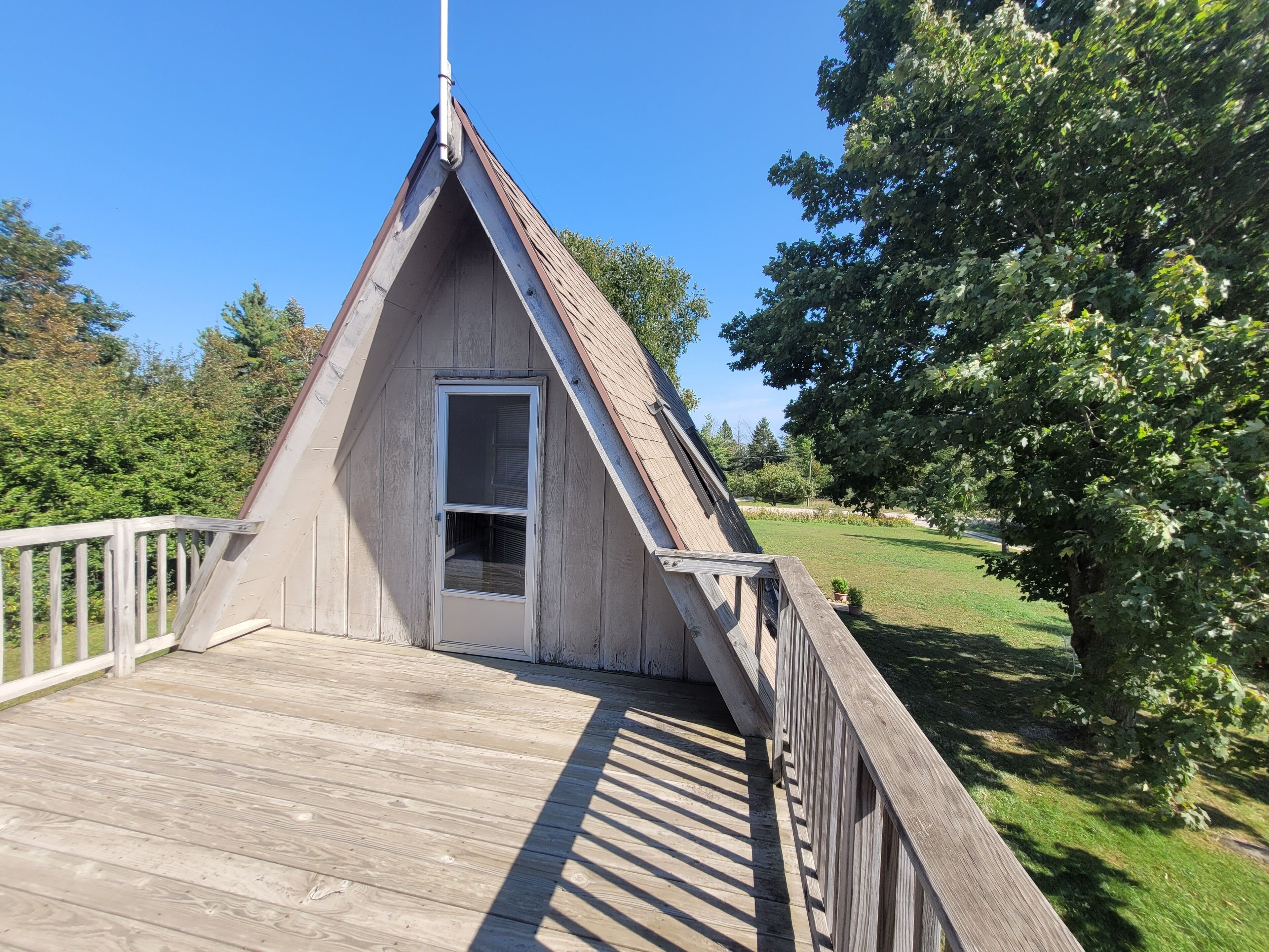 A wooden deck with a triangular roof structure, a door, and a railing.