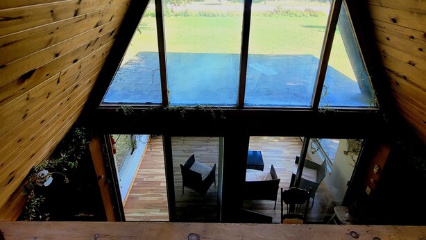 A triangular window with a view of a grassy yard and a wooden deck. - A Frame cabin with a short stroll to a gorgeous sandy beach! (Beaver Island)