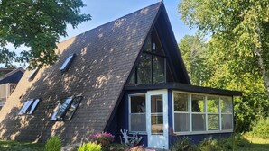 A modern house with a sloped roof, a large window, and a small porch area. - A Frame cabin with a short stroll to a gorgeous sandy beach! (Beaver Island)