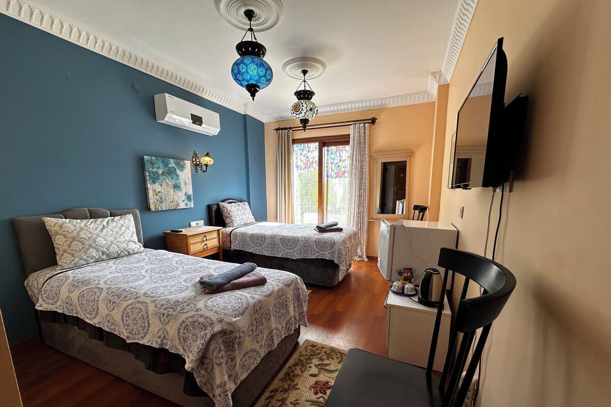 A bedroom with two beds, a desk, a chair, a TV, and a window with curtains.