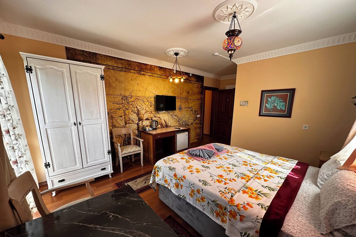 A bedroom with a bed, a desk, a chair, a wardrobe, a map wall, a television, and a ceiling light fixture.