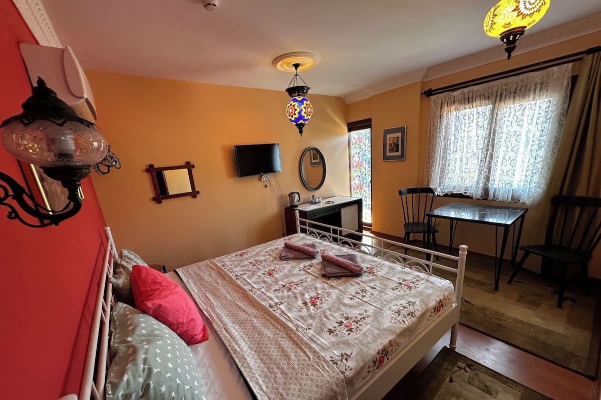A bedroom with a bed, a desk, a chair, a television, and a window with curtains.