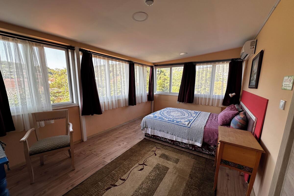 A bedroom with a bed, a chair, a desk, and a window with curtains.