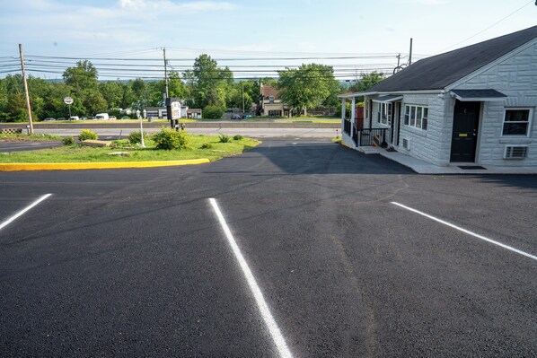 Un motel con una estructura sencilla de un solo piso, un estacionamiento con carriles delimitados y una carretera al fondo.