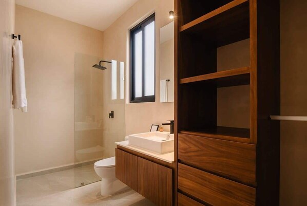 A modern bathroom with a glass shower enclosure, a white sink, and wooden cabinetry.