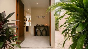 A hallway with a sign reading 'Hacienda Balam,' a wooden door, and a small table with two woven baskets.