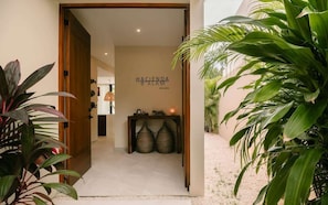 A hallway with a sign reading 'Hacienda Balam,' a wooden door, and a small table with two woven baskets.