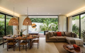 A modern living room with a dining area, a sofa, and a pool view.