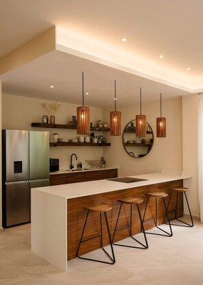 A modern kitchen with a central island, bar stools, stainless steel appliances, and pendant lighting.