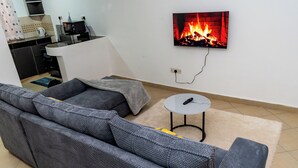 A living room with a grey sectional sofa, a small round table, and a TV displaying a fireplace.