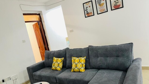 A grey sectional sofa with yellow patterned cushions, a small white table, and a remote control on it.