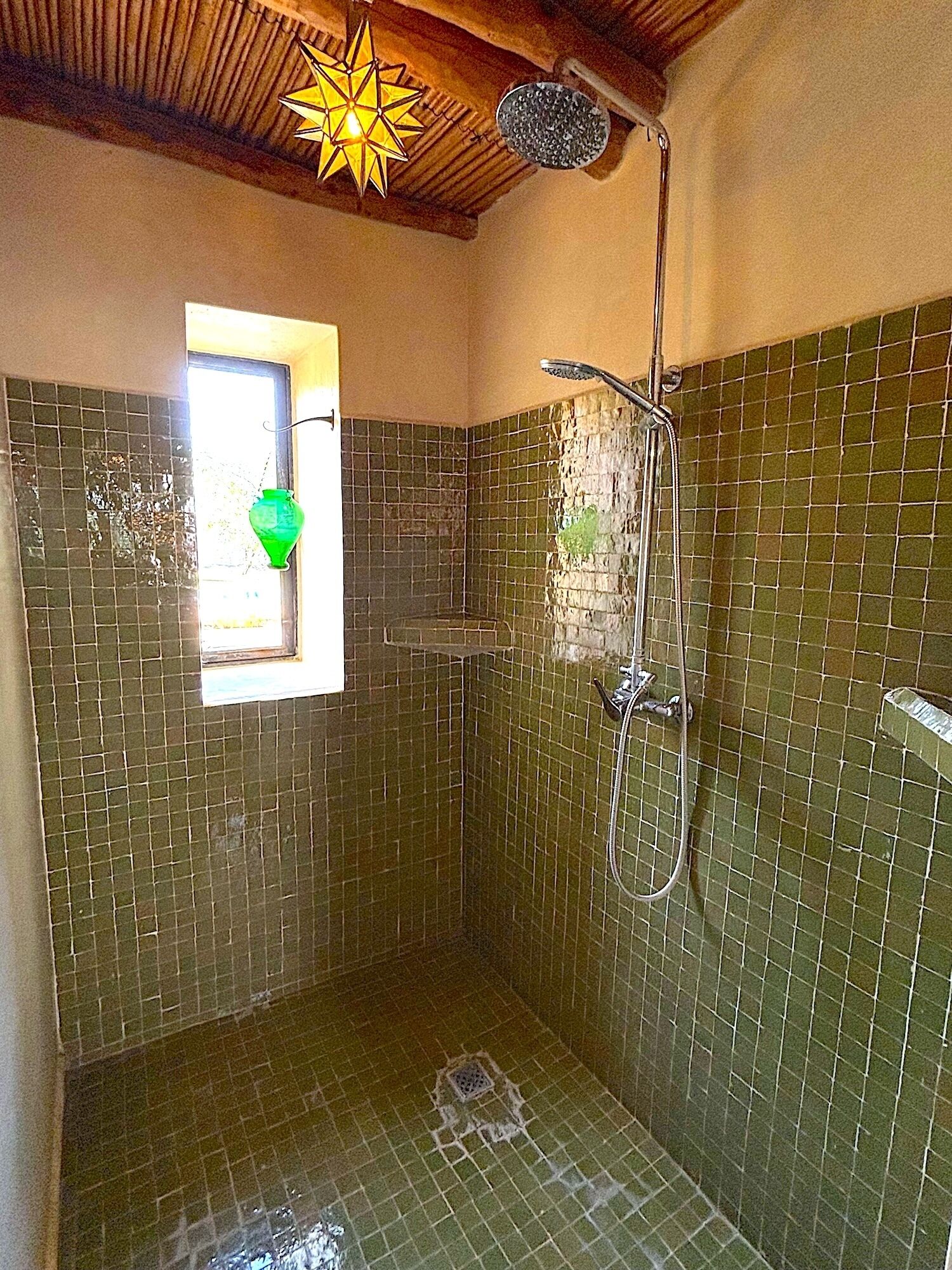 Un baño pequeño con azulejos, una ventana y un cabezal de ducha.