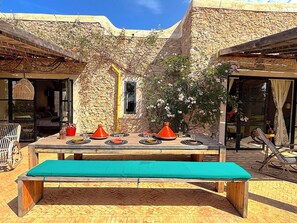 Un espace de restauration en plein air, avec un mur en pierre en arrière-plan, un banc en bois et une table dressée pour deux personnes.