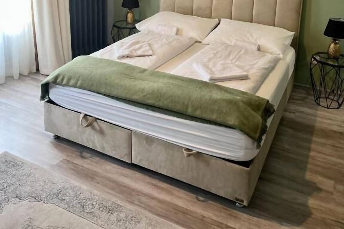 A bedroom with a bed, bedside tables, a lamp, a radiator, and a window with curtains.
