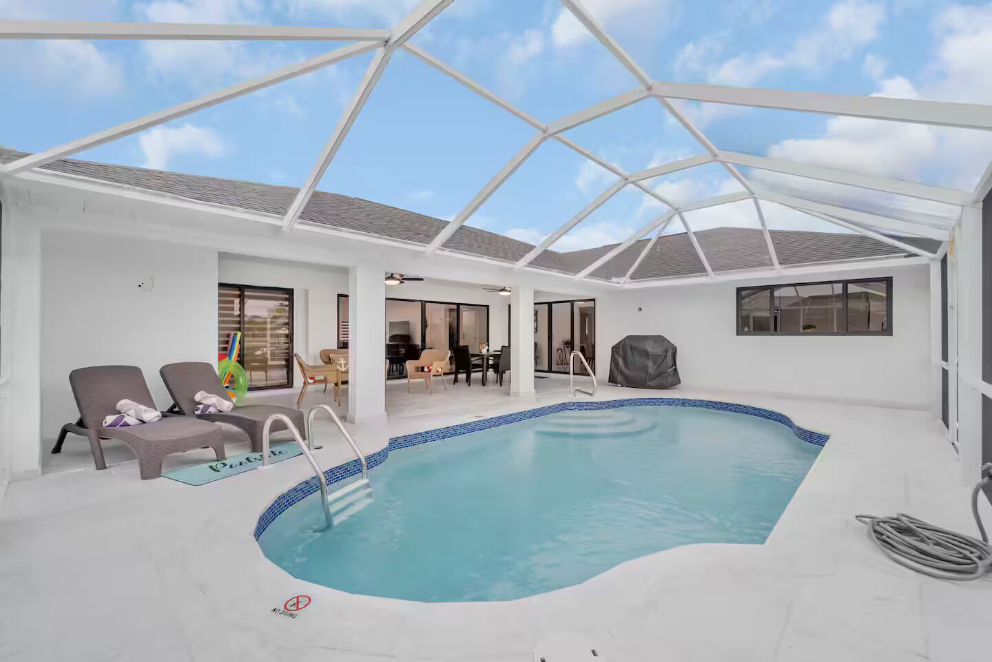 Piscina interior con techo de cristal, sillones de descanso y una parrilla cubierta.