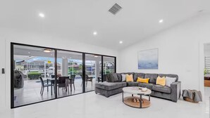 Ein modernes Wohnzimmer mit grauem Sofa, einem Couchtisch und einer Glastür, die zu einem Außenbereich mit Pool und Stühlen führt.