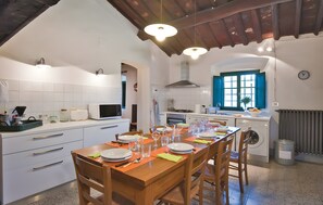 A kitchen with white cabinets, a wooden dining table set for four, a washing machine, and a window with blue shutters.