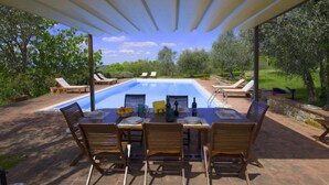 Ein überdachter Essbereich im Freien mit Pool, Holzkunststühlen und einem für eine Mahlzeit gedecktem Tisch.