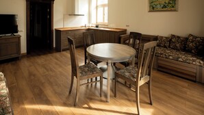 A dining area with a round table, four chairs, a sofa, wooden flooring, a TV, and a window with natural light.