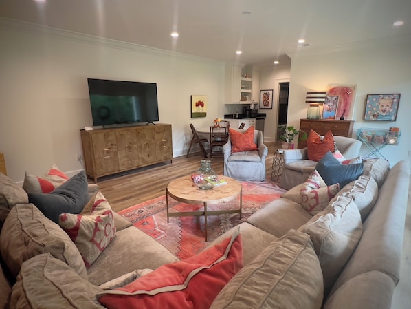 Ein Wohnzimmer mit großem Fernseher, Holzkabinett und einer Couch mit vielen Kissen.