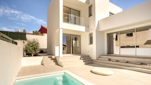 A modern residential building with a swimming pool, outdoor seating, and a staircase leading to a balcony.