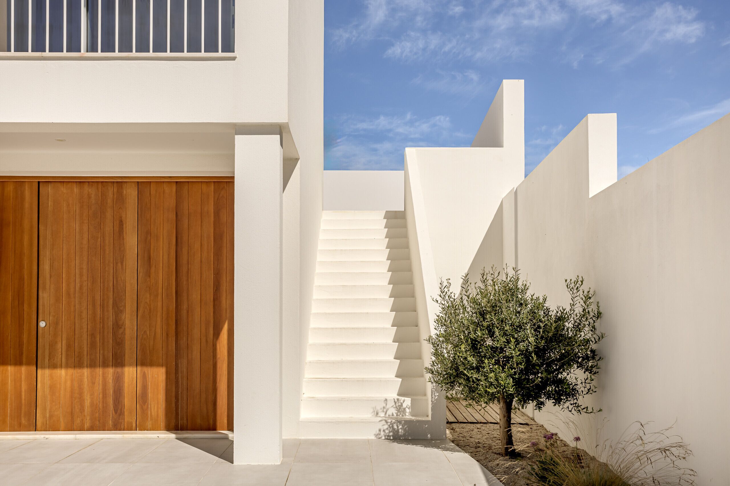 A modern building with a wooden door, white walls, and a staircase leading to a higher level.