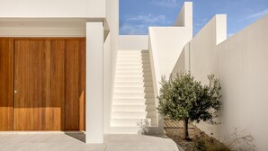 A modern building with a wooden door, white walls, and a staircase leading to a higher level.