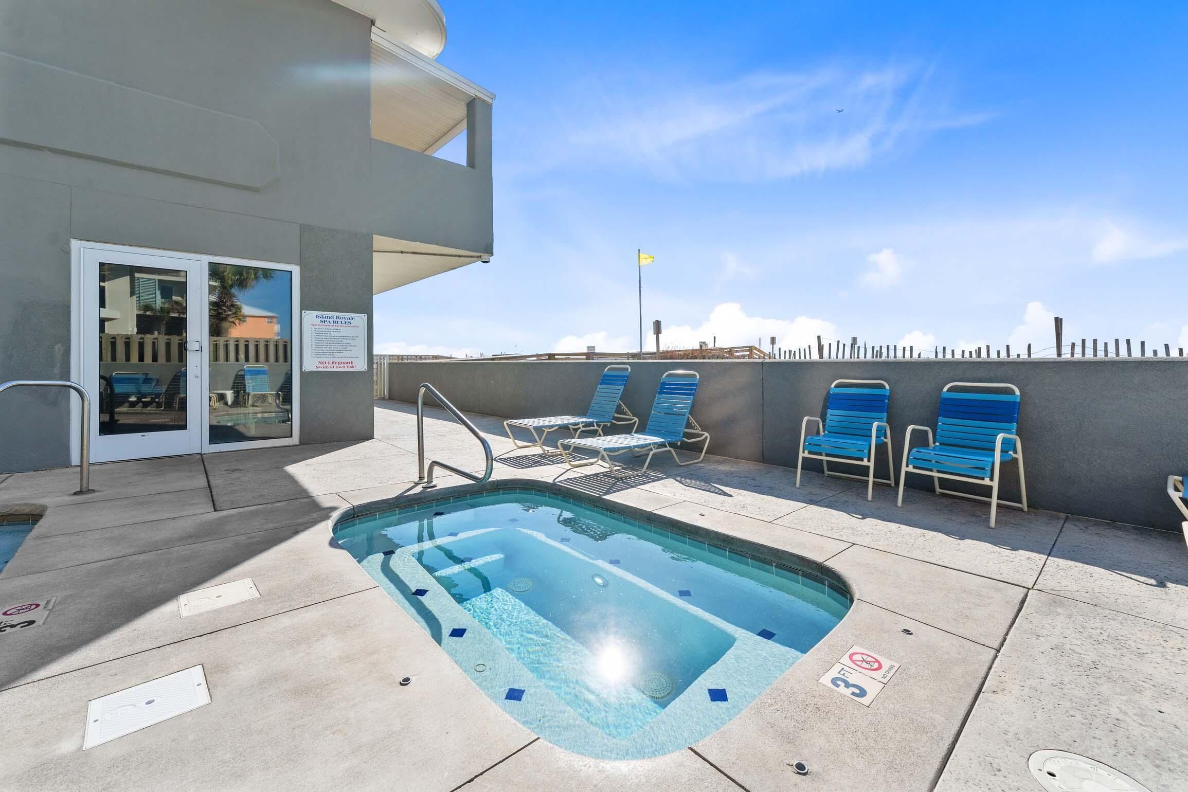 A pool area with a hot tub, lounge chairs, and a building with a glass door.