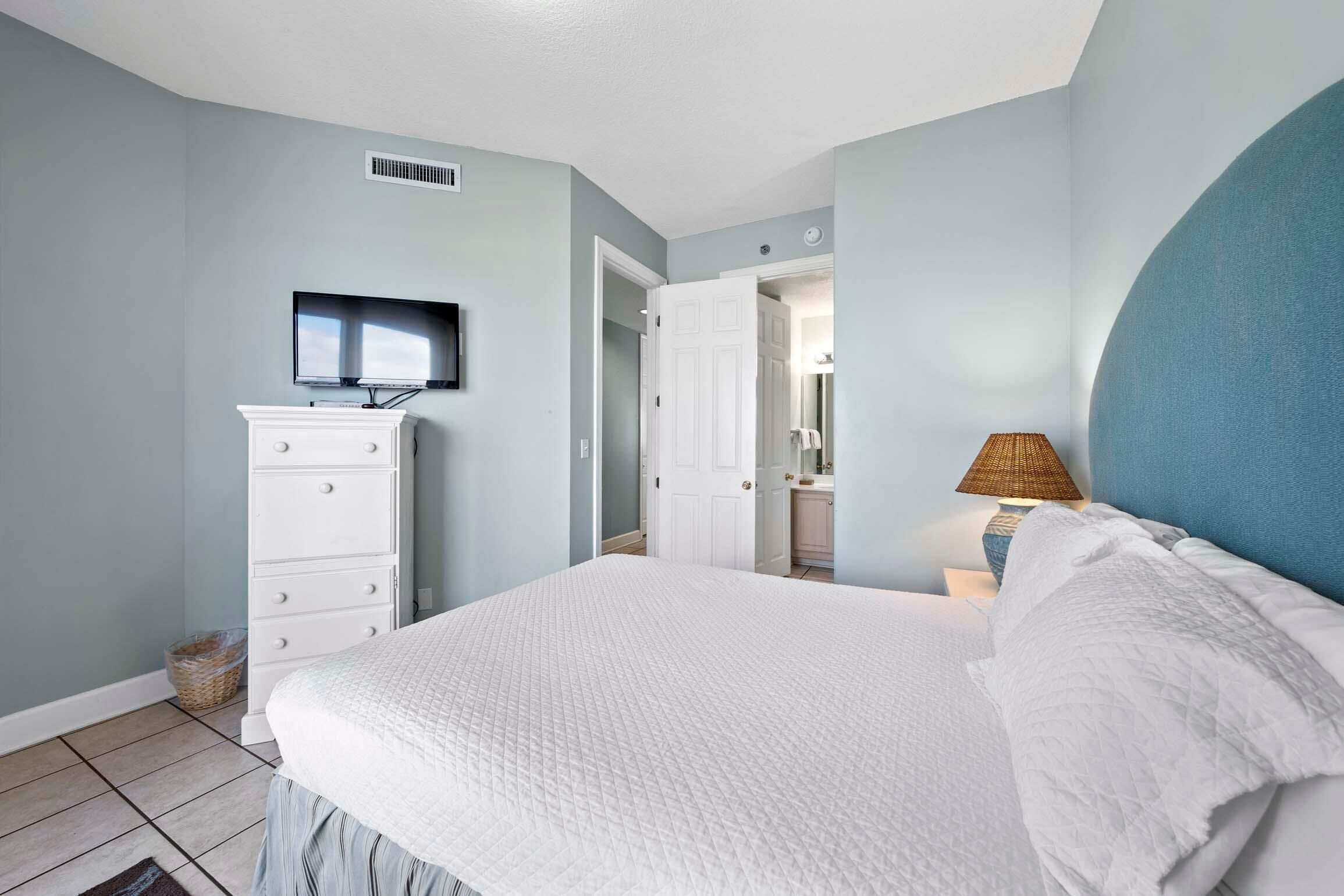 Un dormitorio con cama, cómoda, televisor y lámpara.