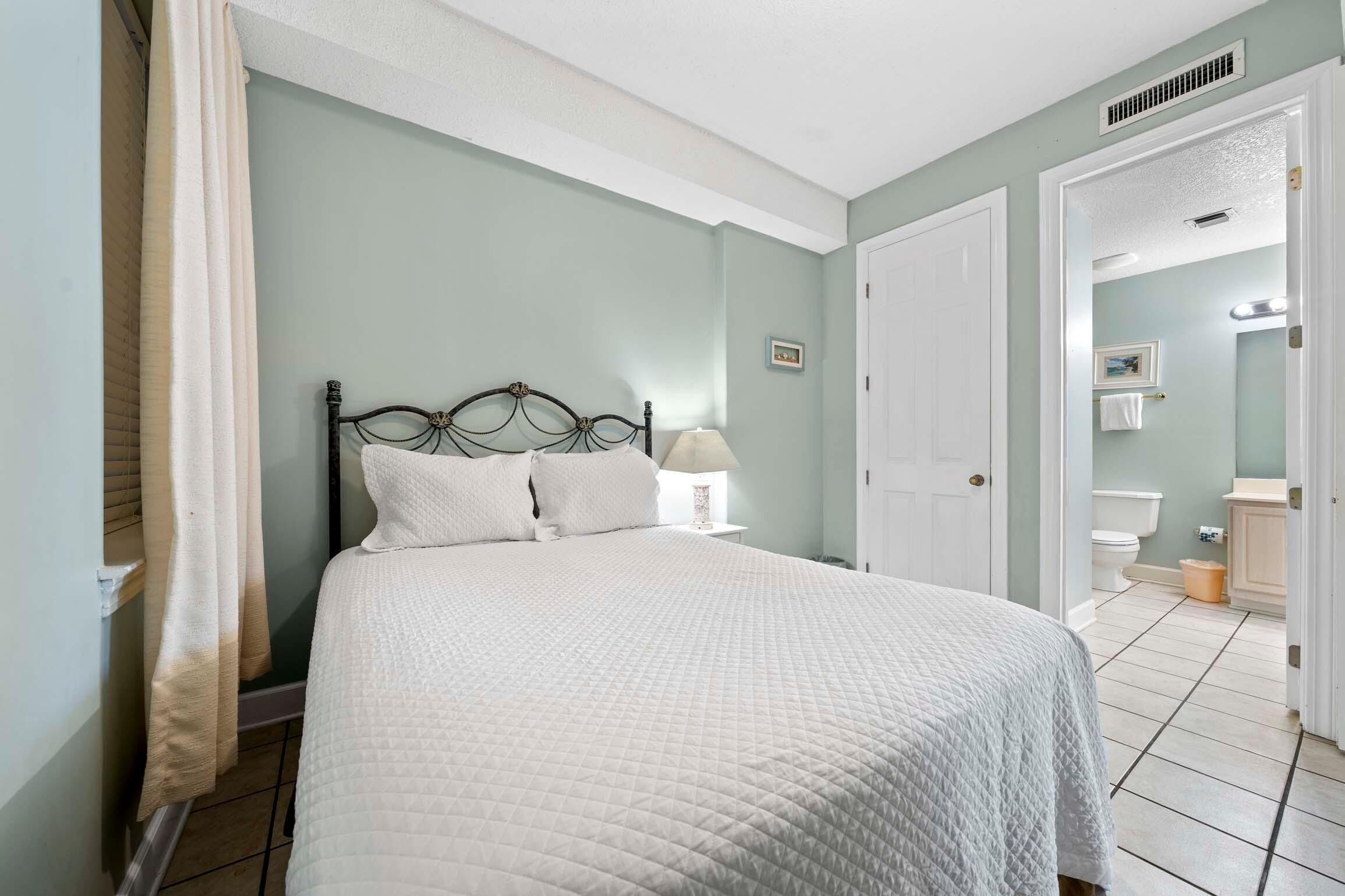 A neatly made bed with a white quilt, a bedside lamp, and a window with curtains.