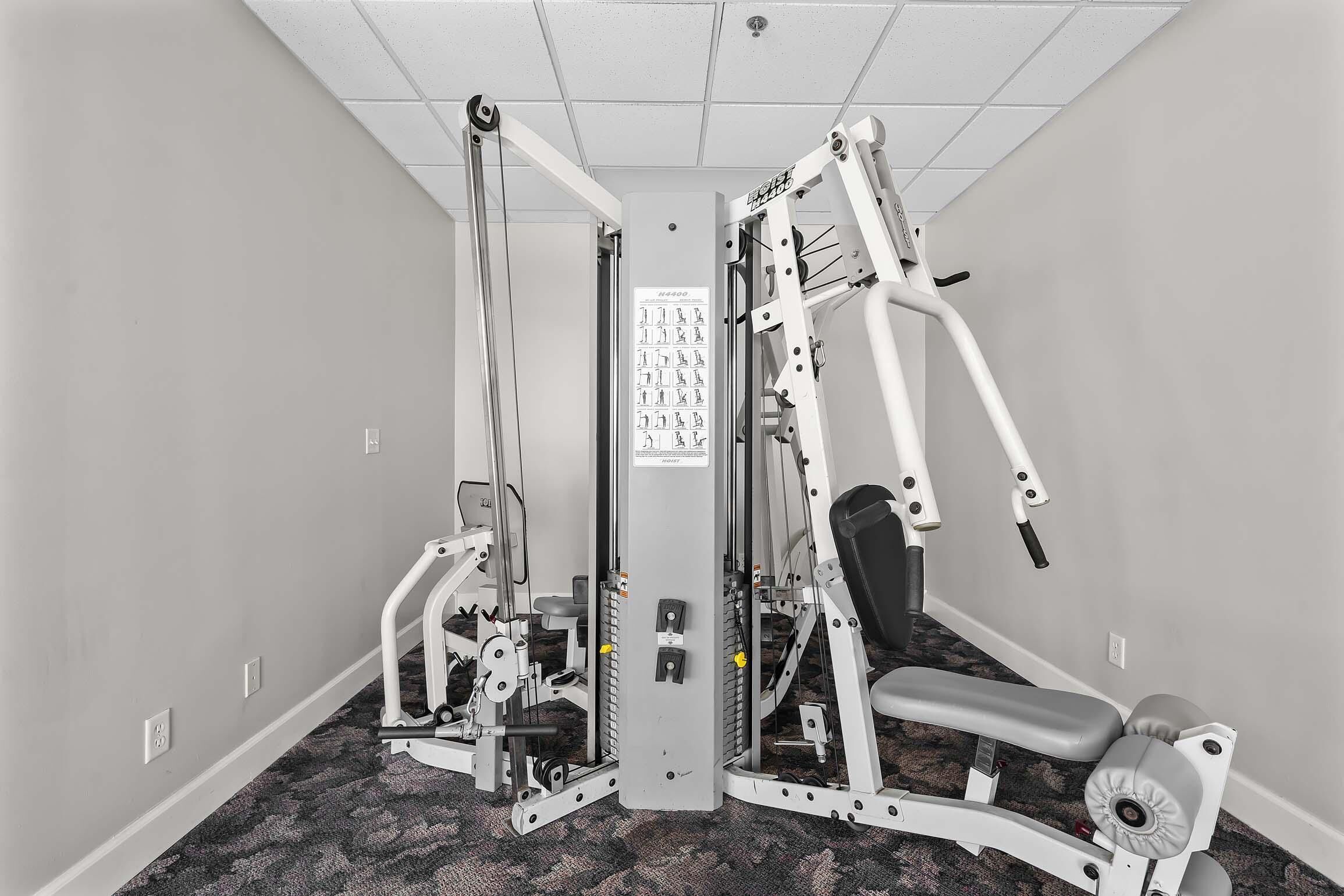 A gym with various exercise machines, a wall-mounted instructional poster, and a carpeted floor.