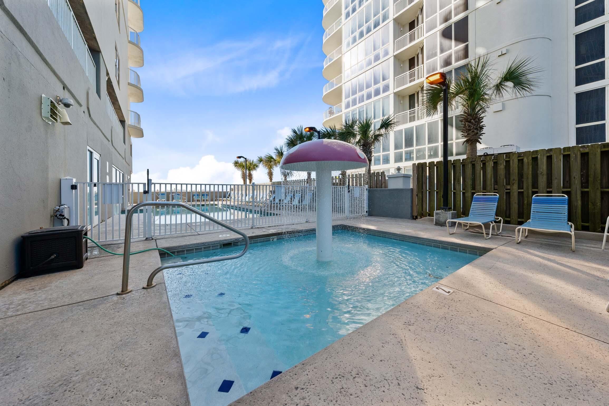 A swimming pool with a water fountain, lounge chairs, and a wooden fence.