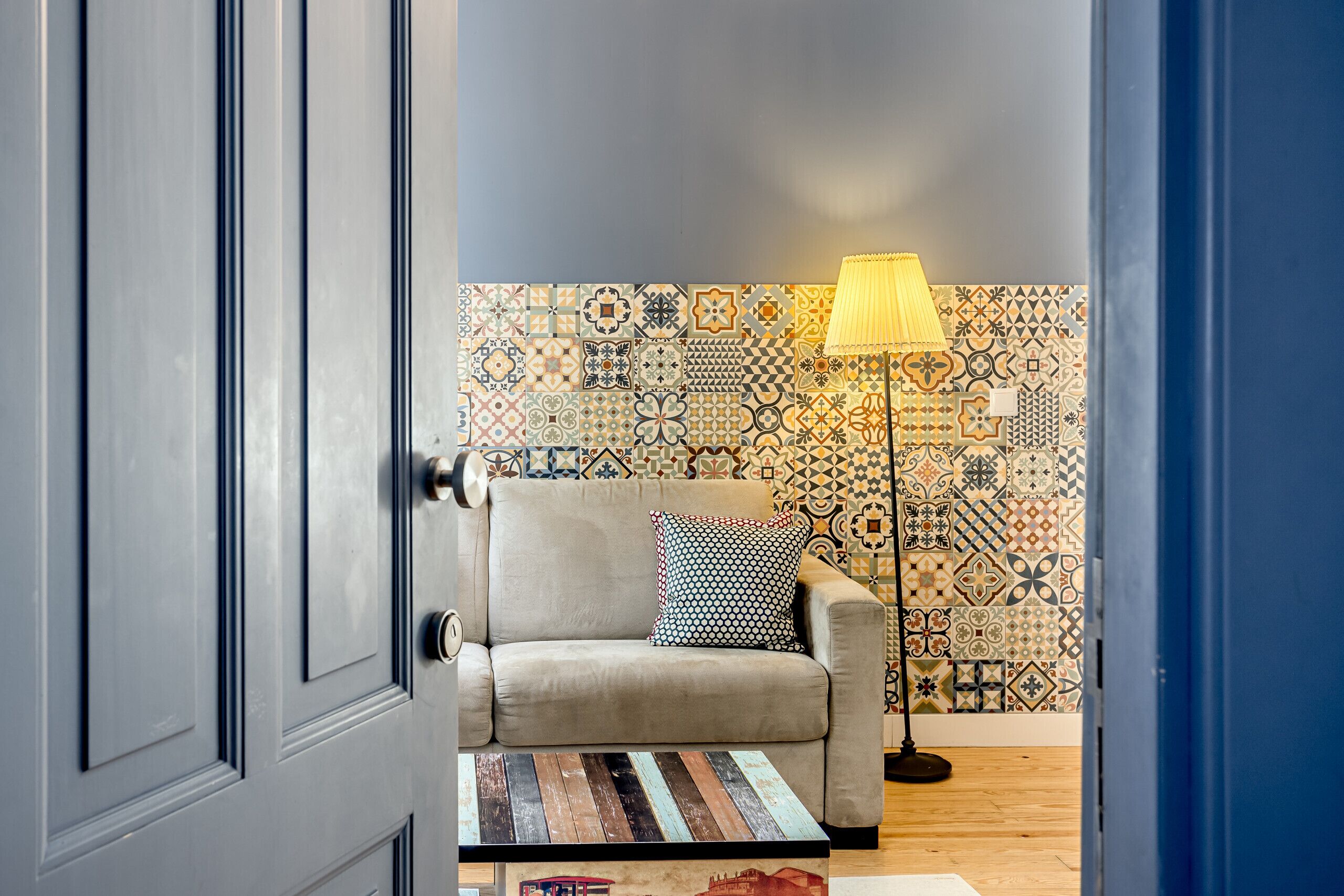 Una stanza con una parete decorata, un divano, una lampada e un tavolo di legno.