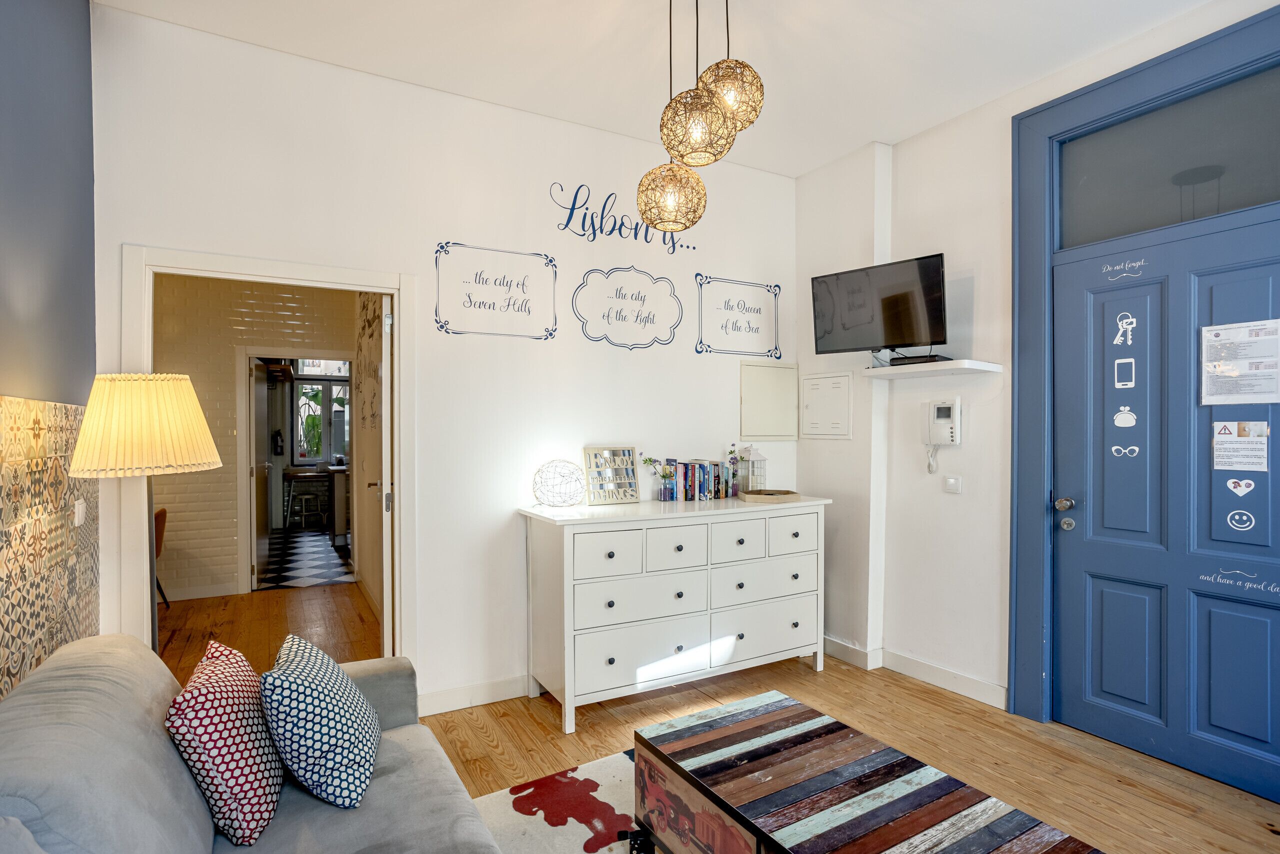 Una sala de estar con un sofá, cojines estampados, un aparador blanco, un televisor y una puerta azul.